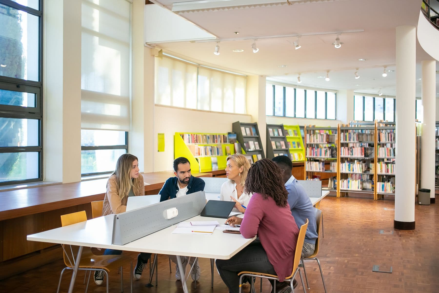Adult learners collaborating around a table with laptops in a library