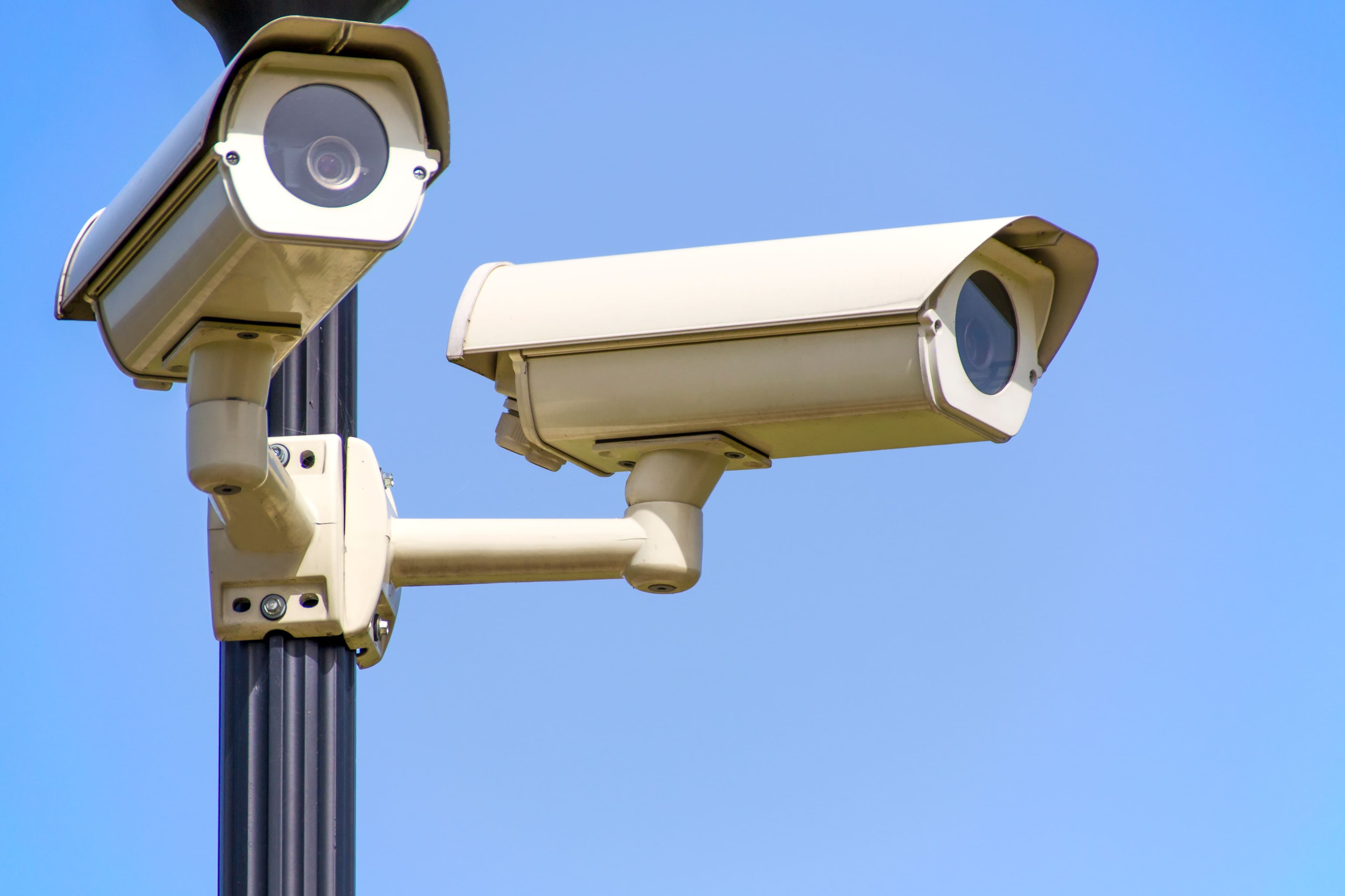 Two CCTV cameras mounted on a post against a clear sky