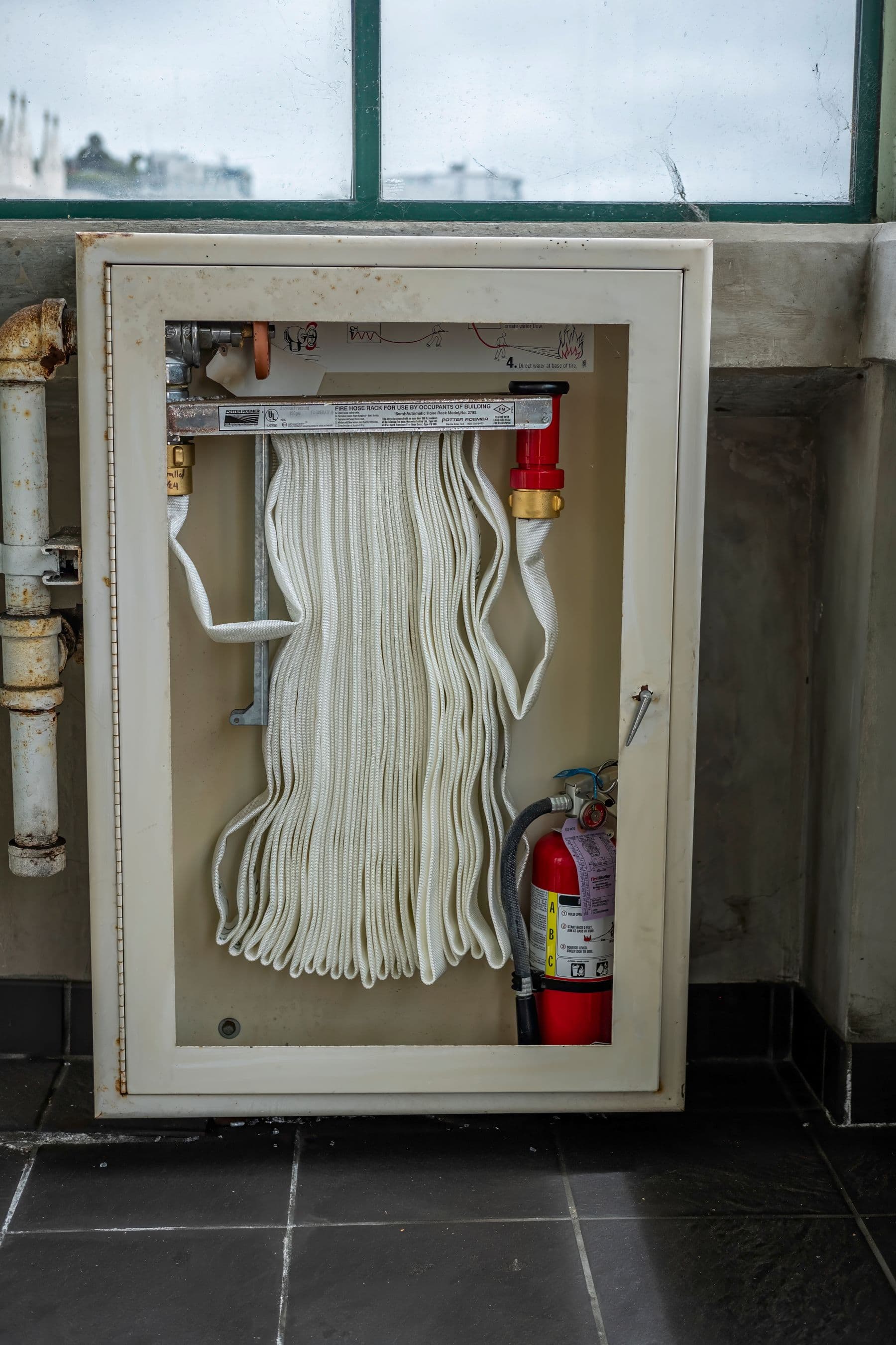 A wall-mounted fire hose cabinet with a red extinguisher